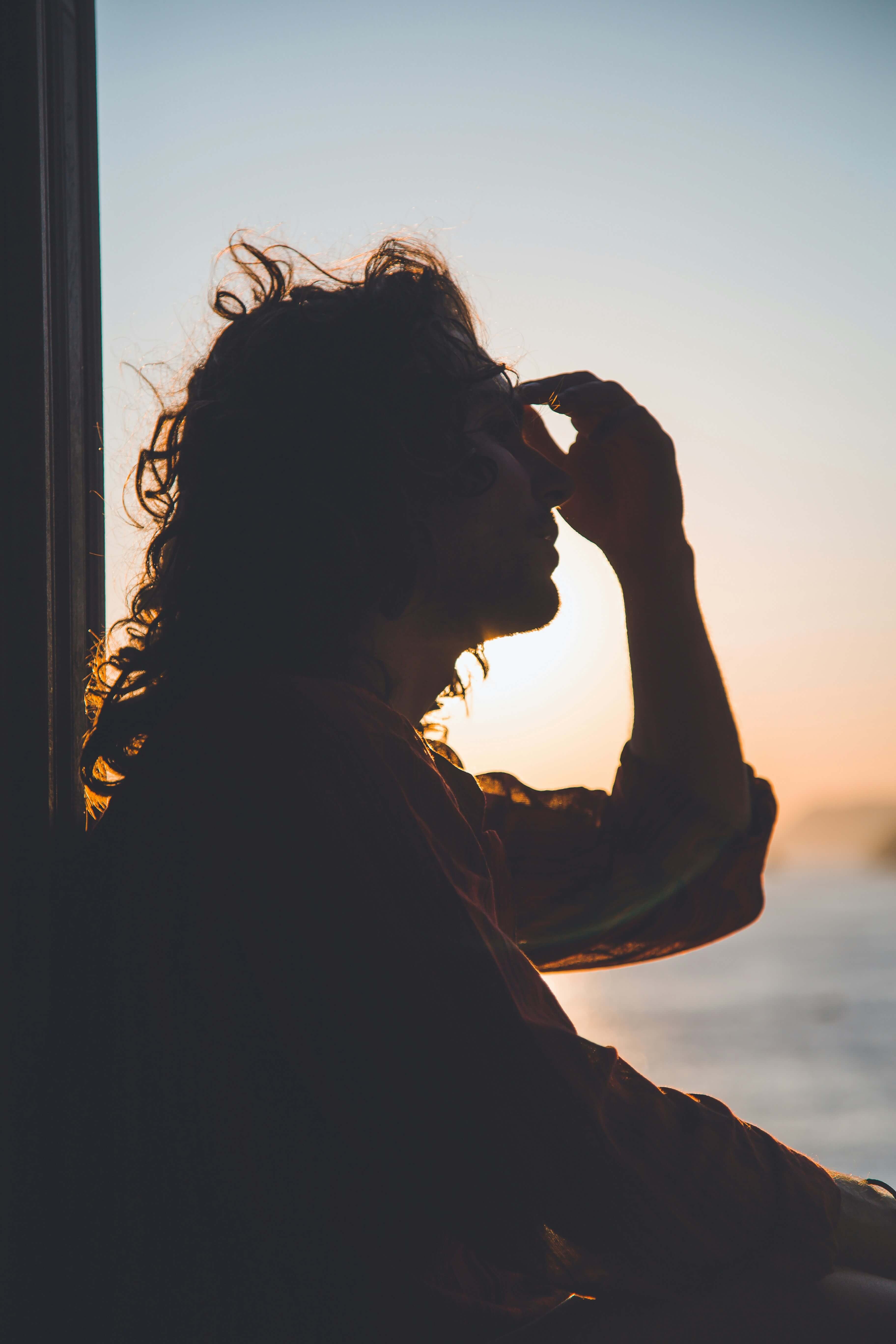 Silhouette of a person at sunset with their hand to their forehead
