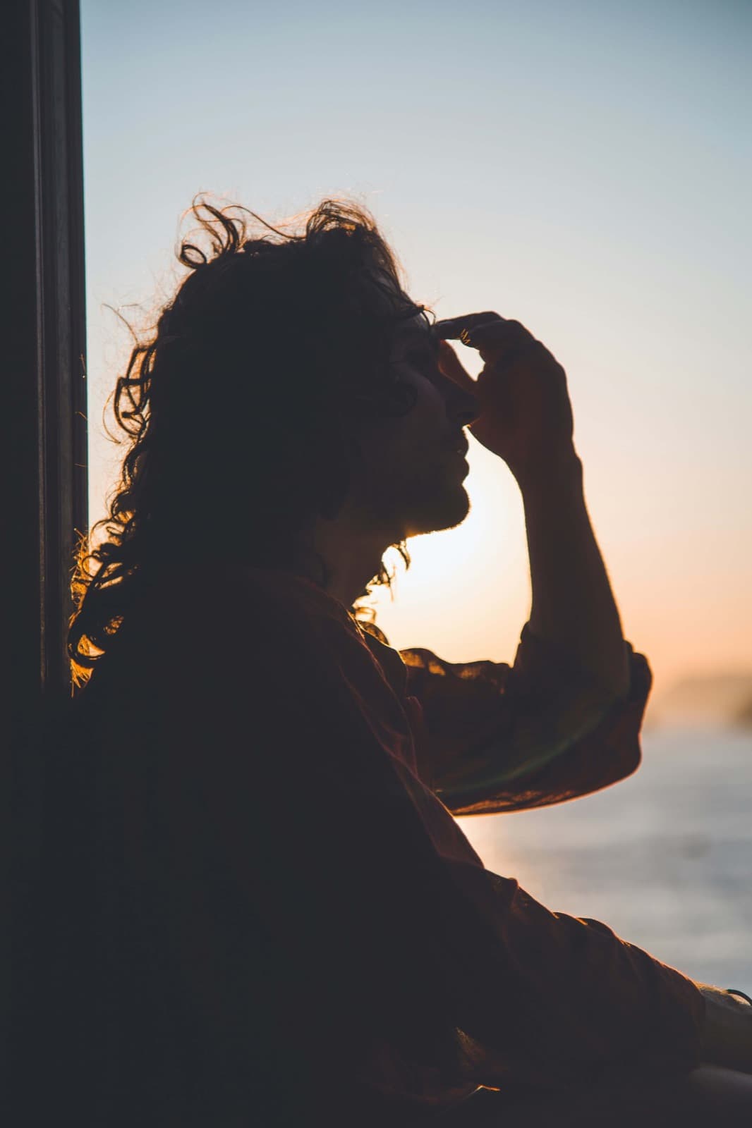 Silhouette of a person at sunset with their hand to their forehead